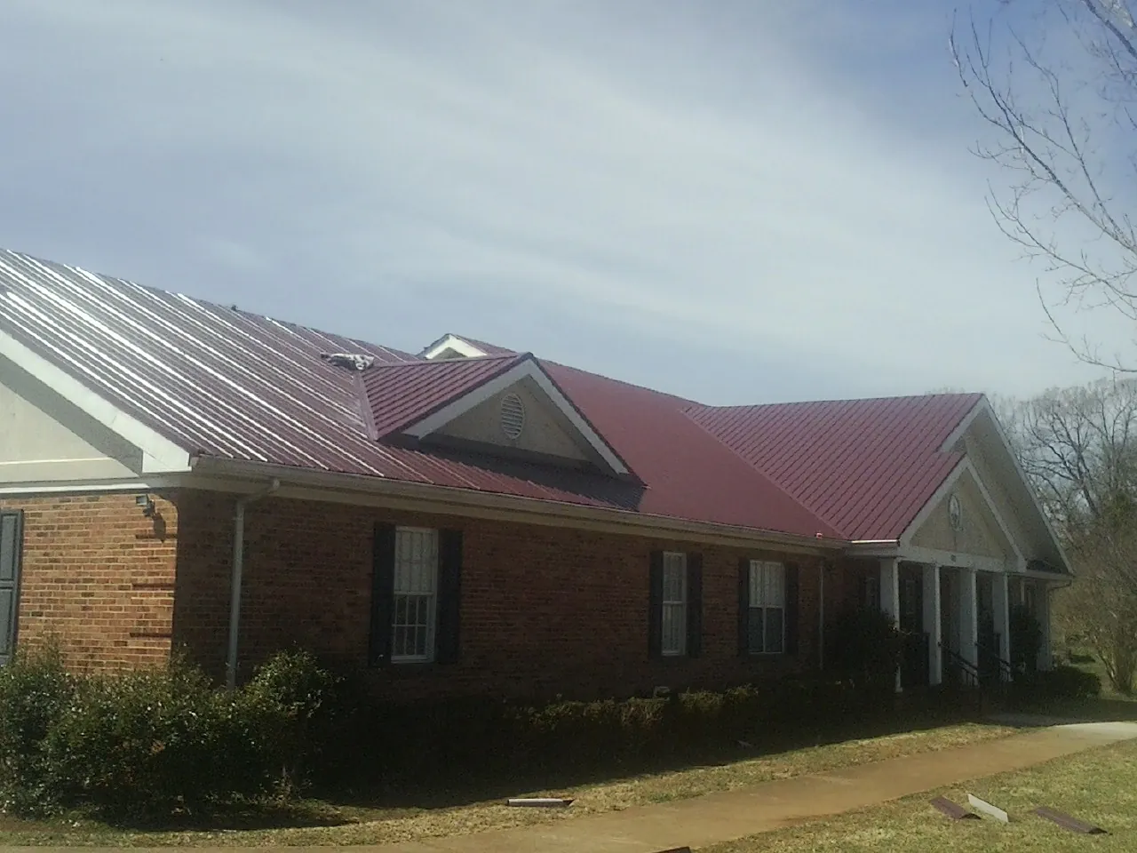 Red metal roof with gabled entries on a long brick building, from a Hail Damage Roof Repair job in Burket
