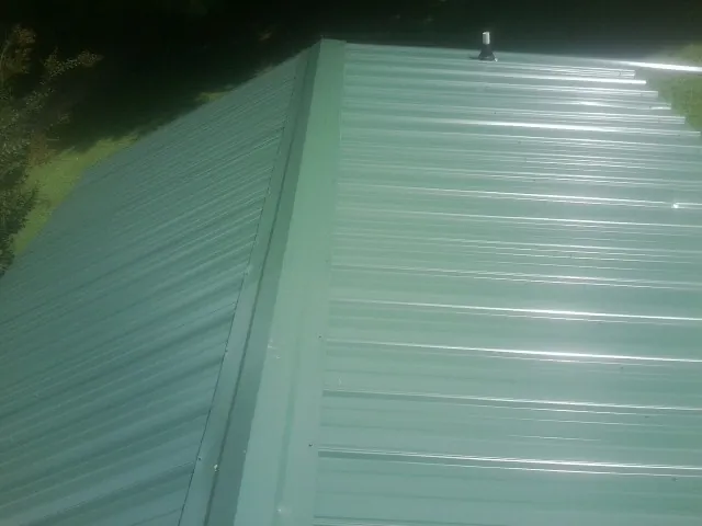 New green metal panels meeting at the ridge of a roof — Flat Roof Repair work by our crew in Burket
