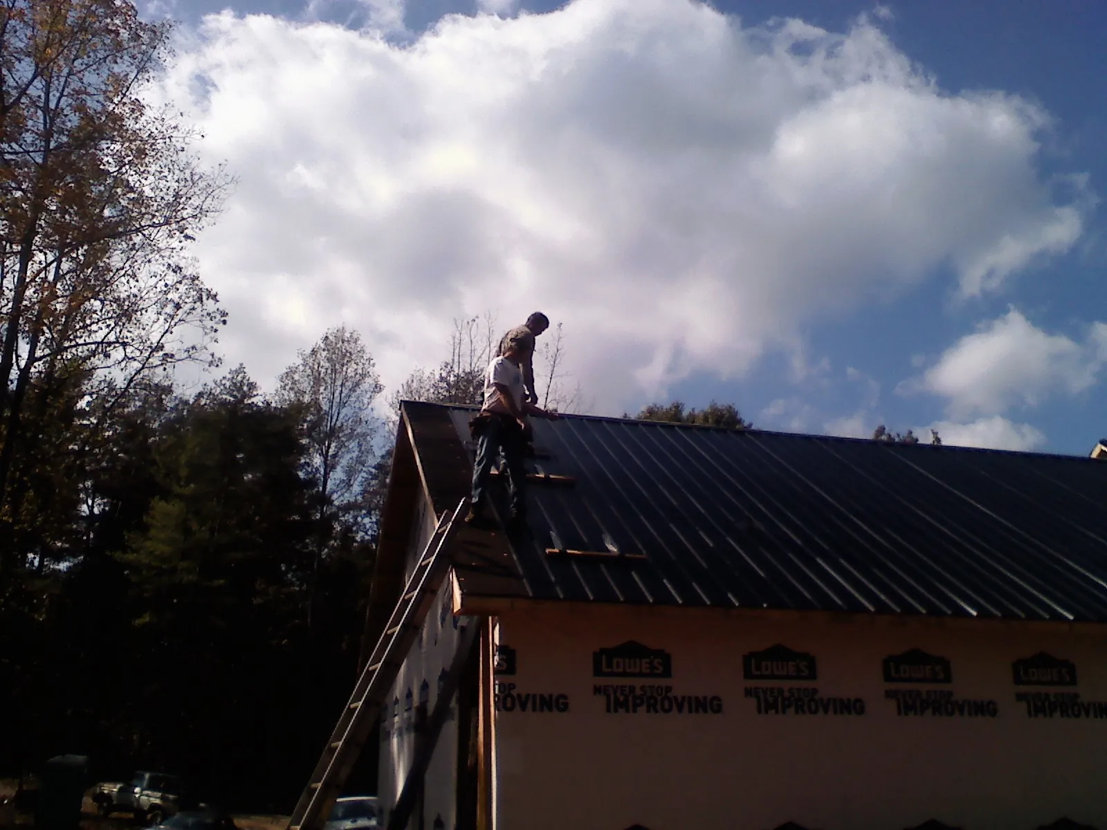 Roofer fastening dark metal panels high against a cloudy sky, from a Roof Inspection job in Burket